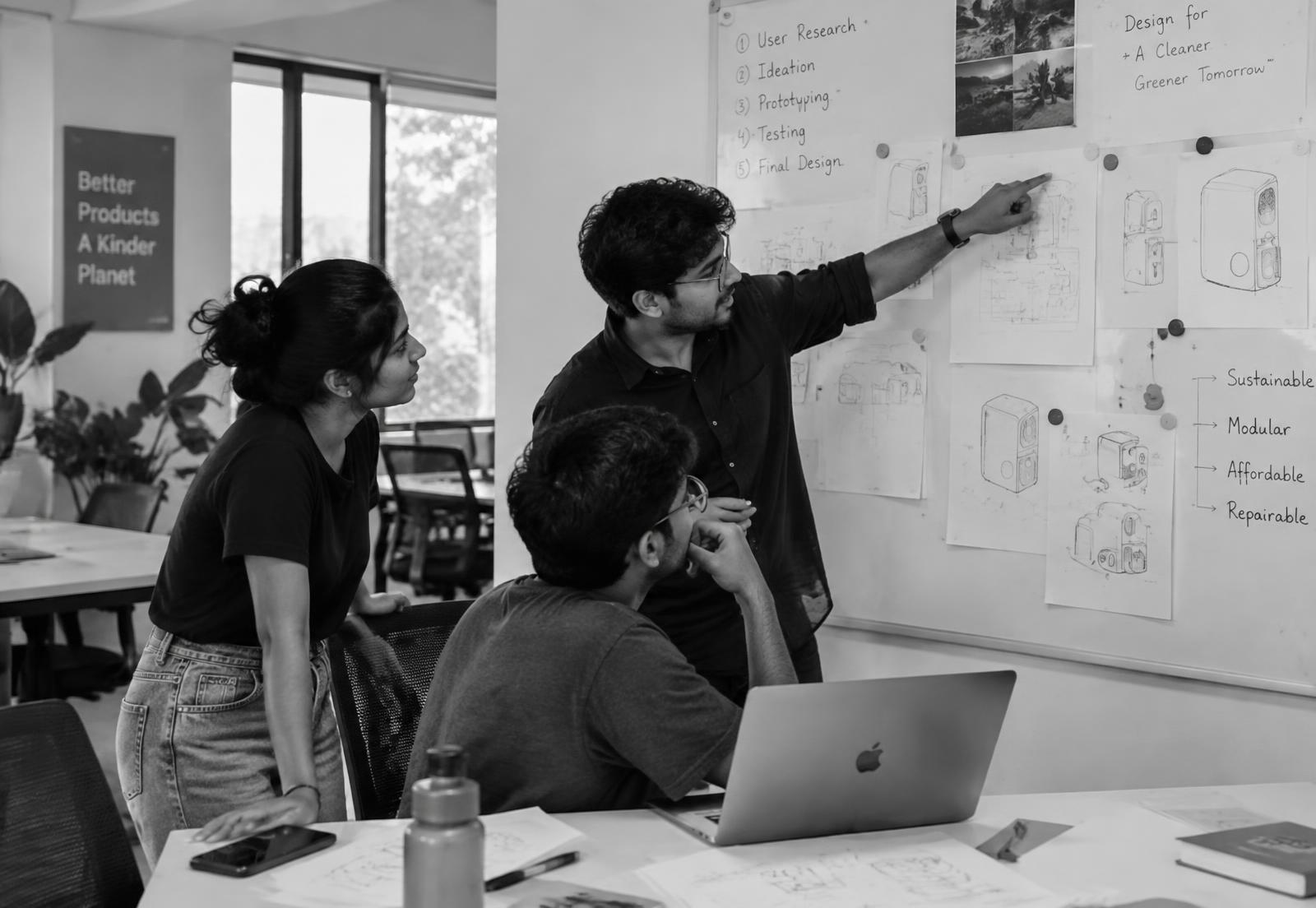Three young people reviewing sketches together at a whiteboard